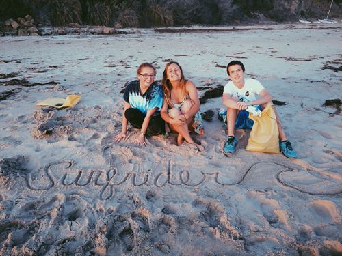 three students sitting on the sand